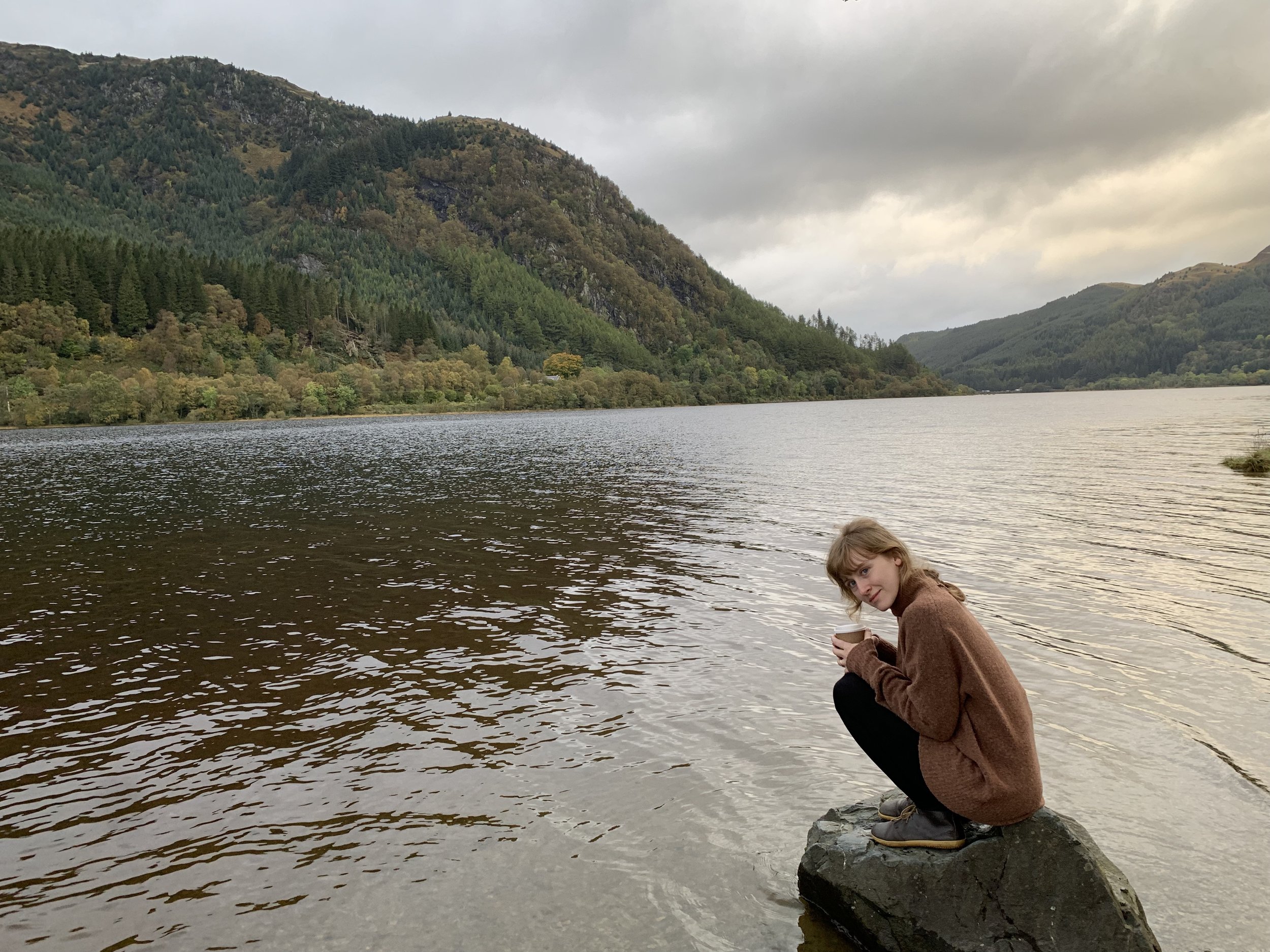 aimee sits on a rock, next to a loch